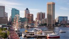 Historical tall ships in the Inner Harbor of Baltimore, Maryland, USA with the city's skyscrapers and buildings in the background.