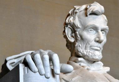 A closeup of the Lincoln Memorial in Washington, DC showing just the president's face and right hand chiseled from stone.