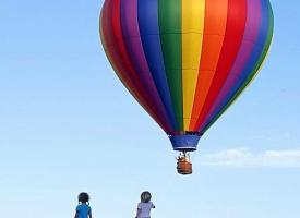 Two children watch a hot air balloon in the sky